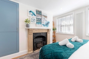 A bedroom with a fireplace, a bed with a teal quilt, and artwork on the wall. - Charming Two Bedroom Apartment in Fairview (Gloucestershire)