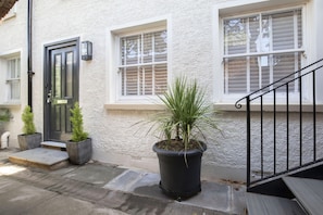 A building with a white exterior, a black door, and a staircase with a black railing. There are potted plants on the ground level. - Charming Two Bedroom Apartment in Fairview (Gloucestershire)