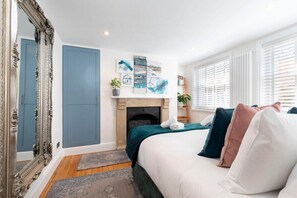 A bedroom with a large ornate mirror, a fireplace, and artwork on the wall.