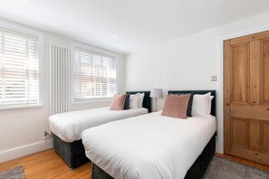 A bedroom with two beds, white bedding, and a wooden door. - Charming Two Bedroom Apartment in Fairview (Gloucestershire)