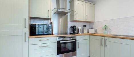 A modern kitchen with light-colored cabinets, a stainless steel range hood, a microwave, a coffee maker, and an oven.