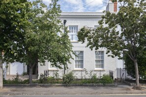 A two-story house with a white exterior, a visible garage door, and a small front yard with trees and a fence.