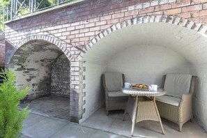 A patio area with a brick archway, wicker furniture, and a small table with cups and a glass.
