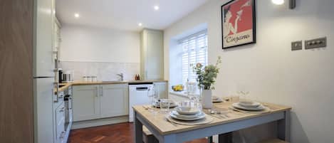 A modern kitchen with white cabinetry, a dining table set for four, and a window with blinds.