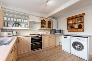 Een kleine keuken met houten kastjes, een inbouwoven, een magnetron en een wasmachine.