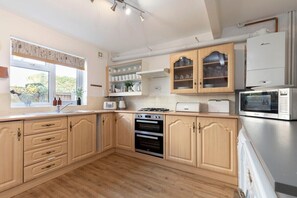 Een moderne keuken met houten kastjes, een inbouwoven, een magnetron en een raam met uitzicht op groen.
