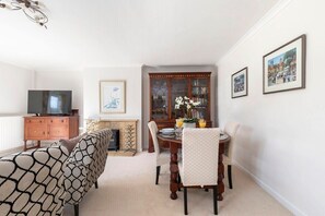 Un coin repas avec une table en bois, des chaises et une cheminée. On y trouve également un téléviseur posé sur un meuble en bois et un tableau encadré accroché au mur.