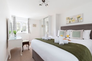 Een hotelkamer met een bed, nachtkastje, spiegel, raam met gordijnen en een schilderij aan de muur.