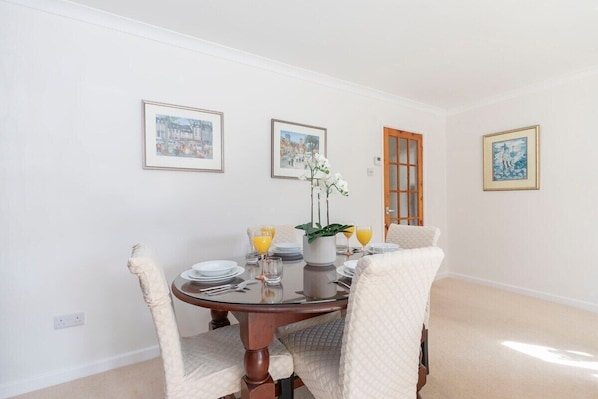 A dining room with a round table set for four, white chairs, and framed pictures on the walls.