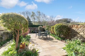 A patio with stone flooring, a table with chairs, and surrounding greenery.