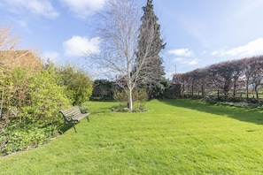Un jardin bien entretenu, avec un banc, une variété d’arbres et un ciel dégagé.