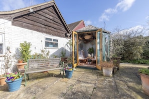 Une maison de campagne avec un banc en bois, des plantes en pot et un petit jardin.
