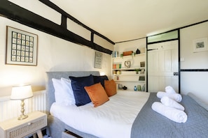 Une chambre à coucher bien rangée, avec un lit, des oreillers, une table de chevet et une étagère contenant des livres et des objets décoratifs.