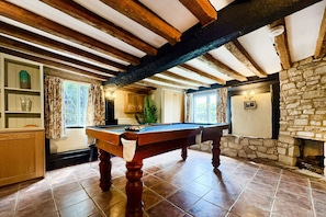 A pool table in a room with exposed wooden beams, stone walls, and a fireplace. - Beautiful 4 Bedroom Cotswold Thatched Cottage (Twigworth)