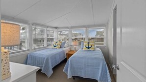 A room with two beds, each with striped bedding and anchor pillows, a small table with a lamp, and large windows with blinds. - Normandy Beach Getaway! Spacious 2-Family Home. Perfect for Families & Friends (Lavallette)