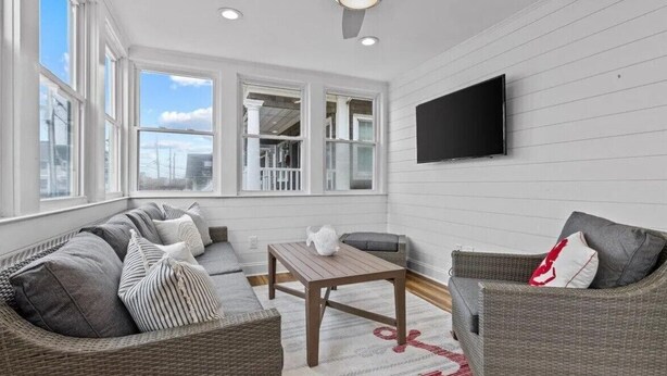 A sunlit room with a sofa, a table, and a television mounted on the wall. - Normandy Beach Getaway! Spacious 2-Family Home. Perfect for Families & Friends (Lavallette)