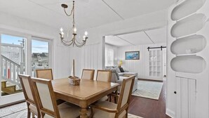 A dining area with a wooden table and chairs, a chandelier, and a view of the outside. - Normandy Beach Getaway! Spacious 2-Family Home. Perfect for Families & Friends (Lavallette)