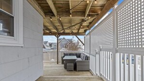 A covered outdoor deck with a seating area, wooden beams, and string lights. - Normandy Beach Getaway! Spacious 2-Family Home. Perfect for Families & Friends (Lavallette)
