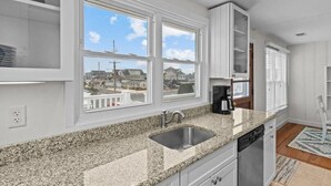 A kitchen with granite countertops, a stainless steel sink, white cabinetry, and large windows offering a view of a residential area. - Normandy Beach Getaway! Spacious 2-Family Home. Perfect for Families & Friends (Lavallette)