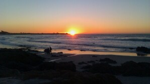 Um pôr do sol sobre uma praia com pedras em primeiro plano.