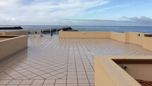 Um terraço no telhado com piso de azulejos, áreas de estar e vista para o mar.