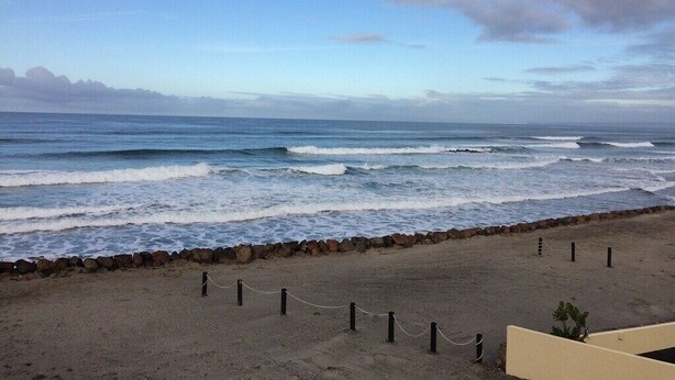 Uma praia com ondas, um muro de pedra e uma barreira de corda.
