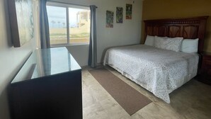 Quarto com cama, ventoinha no teto, escrivaninha e janela com cortinas.