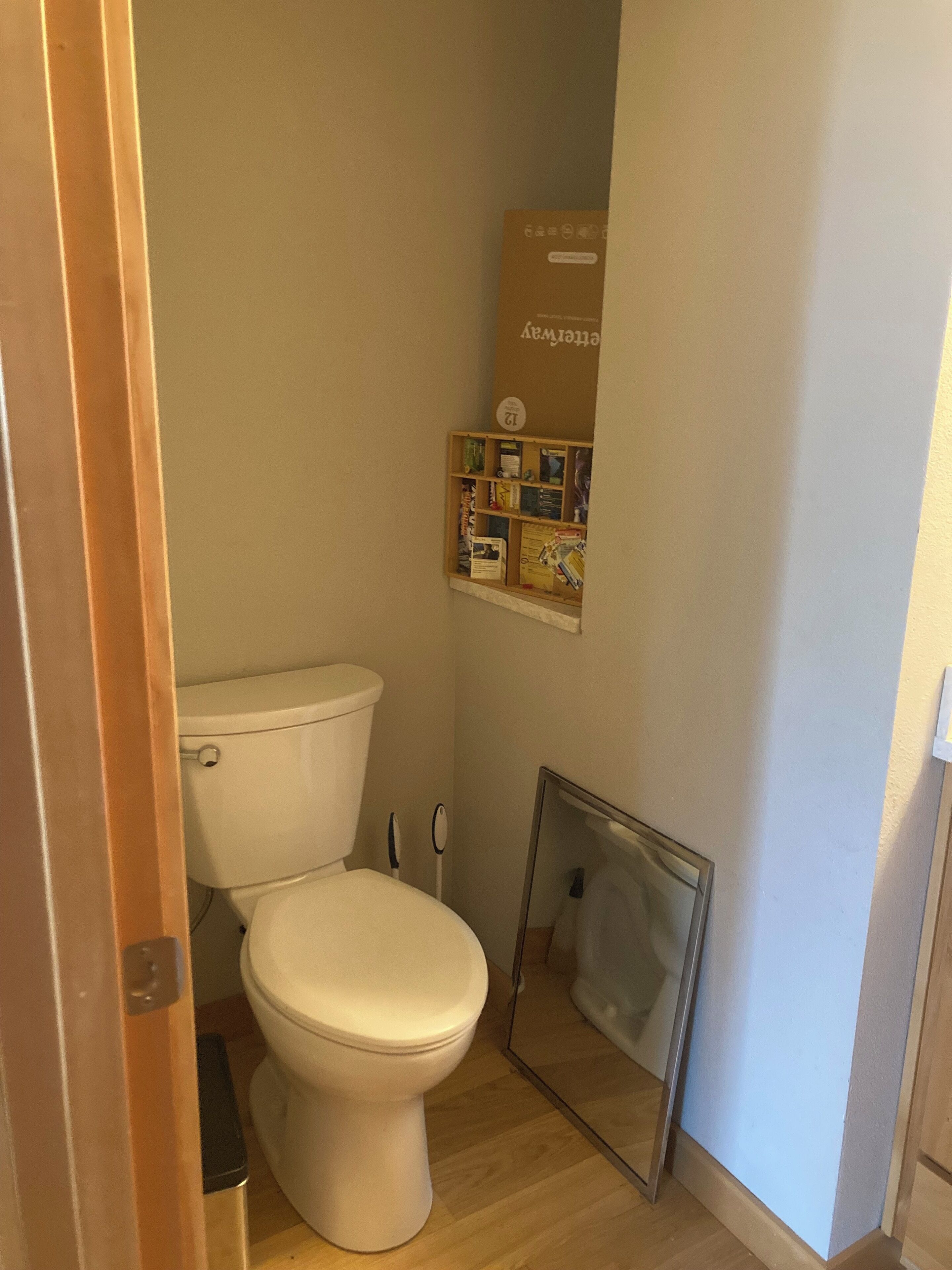 A small, compact bathroom with a white toilet, a wooden floor, and a wall-mounted shelf with various items.