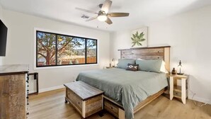 A bedroom with a large window, a ceiling fan, a bed with pillows, a bedside table, and a wooden bench. - Sedona Stargazer Retreat w/ Spa! (Sedona)