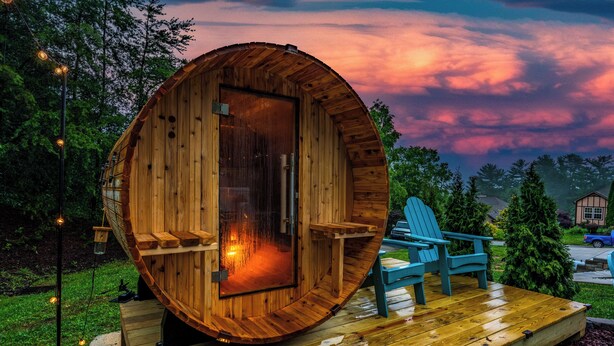A wooden cabin with a circular door, a deck with chairs, and a visible fireplace. - Game Room, Hot Tub, Cold Plunge, Sauna, Fire Pit (Asheville)