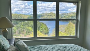 A bedroom with a large window offering a view of a lake and forest.