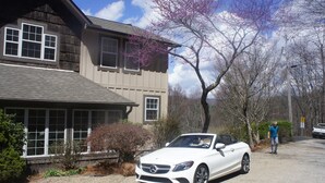A white convertible car parked in front of a two-story house with a garage.