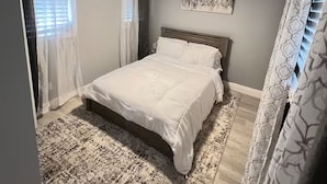 Een slaapkamer met een bed, een plafondventilator, een vloerkleed en gordijnen.