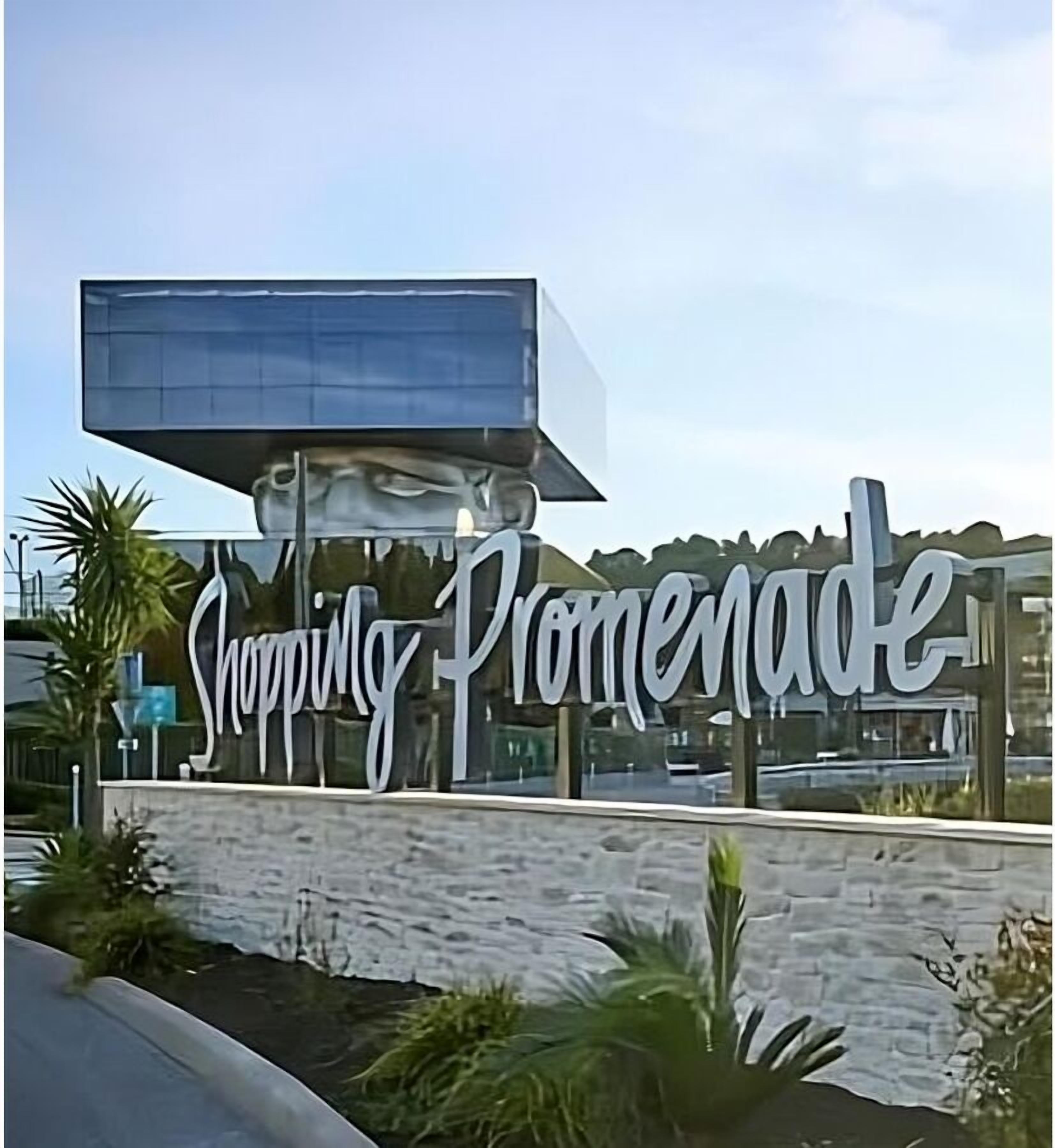 Placa para 'Shopping Promenade', com design moderno e uma grande estrutura de vidro acima.