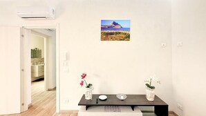 Een moderne kamer met een houten vloer, een donker houten tafel met twee bloemenvazen, een schilderij aan de muur, en een uitzicht op een badkamer door een open deur.