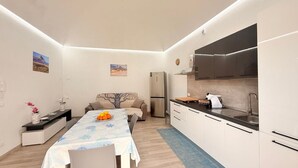 Een kleine keuken met moderne apparaten, een eetgedeelte met een tafel voor twee personen, en een bank.
