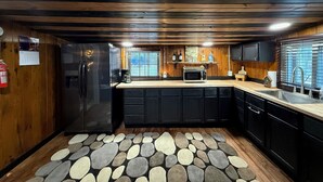 A modern kitchen with wooden paneling, a stone-patterned rug, a refrigerator, a microwave, and a sink.