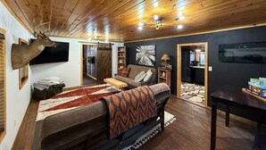 A cozy room with a bed, a desk, a television, and a deer head mounted on the wall.