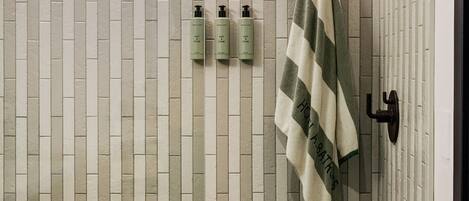 A bathroom with a tiled wall, a towel hanging on a rack, and three bottles of shampoo and conditioner on the wall.