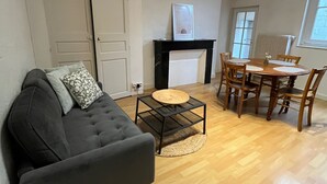 Un salon comprenant un canapé, une table basse, une cheminée, une table à manger avec des chaises et une grande fenêtre.