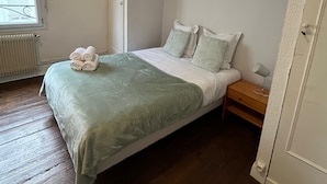 Une chambre à coucher comprenant un lit, une table de chevet, une fenêtre avec des stores et un radiateur.