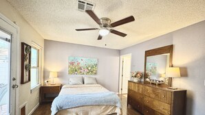A bedroom with a bed, nightstands, a dresser, a ceiling fan, and a window. - Cozy 2-bedroom house in Henderson with WiFi, AC, Solar (Henderson)