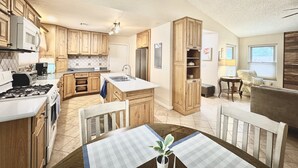 A spacious kitchen with wooden cabinets, a central island, and a dining area with a table and chairs. - Cozy 2-bedroom house in Henderson with WiFi, AC, Solar (Henderson)