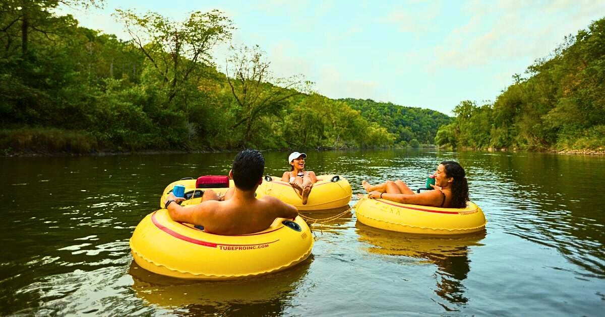 Three people floating on yellow tubes in a river surrounded by greenery.