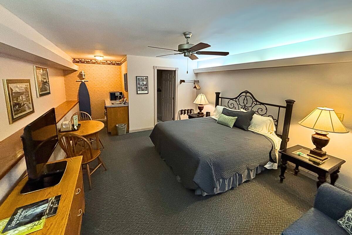 A hotel room with a bed, desk, chair, and a ceiling fan.