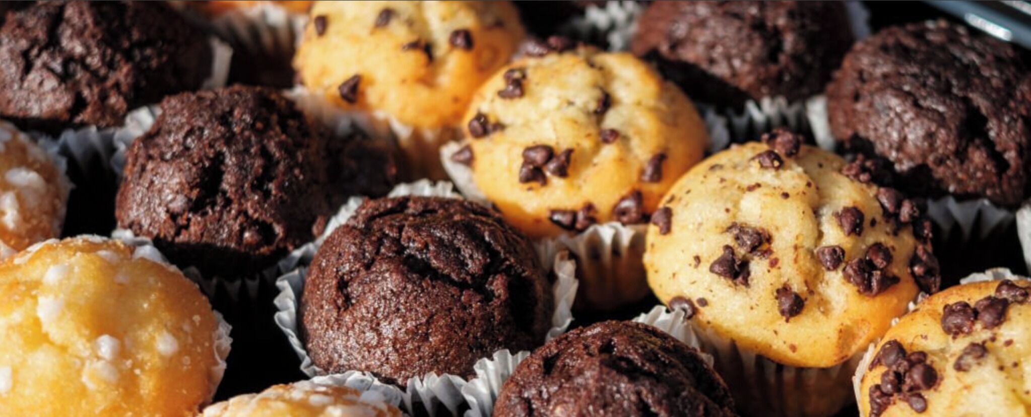 A variety of muffins in paper cups, some with chocolate chips.