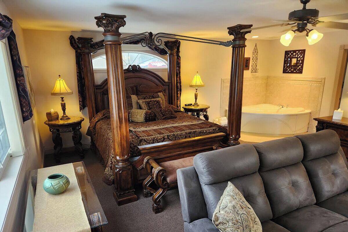 A bedroom with a four-poster bed, a sitting area with a sofa, a small table with a vase, and a bathtub.