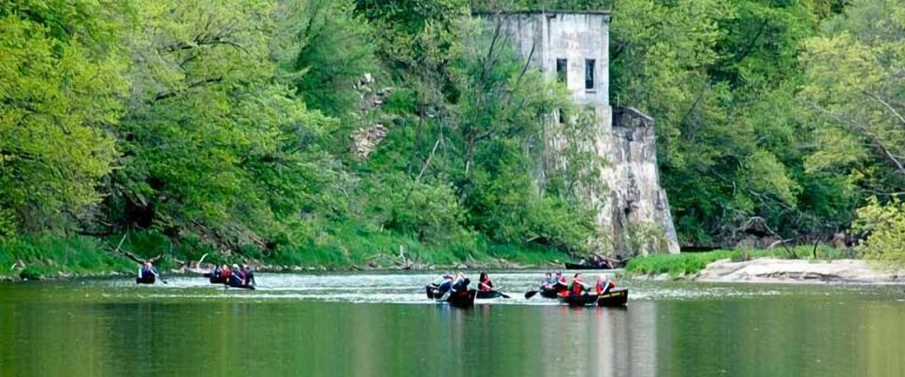 A group of people in a boat on a river surrounded by dense greenery and a stone structure.