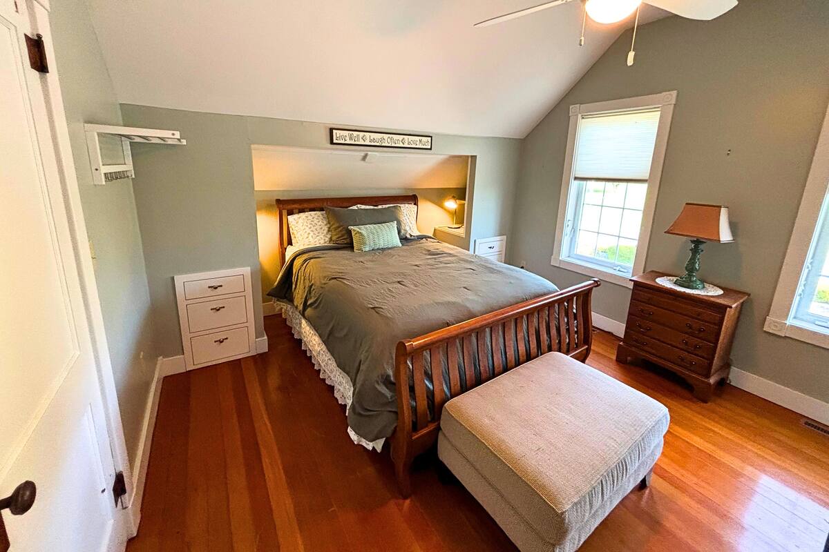 A bedroom with a bed, a nightstand, a dresser, a window, and a ceiling fan.