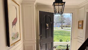 A hallway with a bench, a dark door with a cat-shaped handle, and a view of a green lawn.